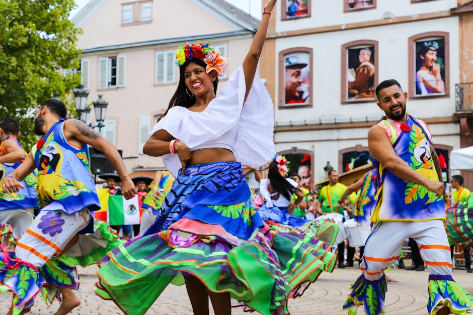 Dancers in colorful traditional attire perform energetically in a lively urban town square.